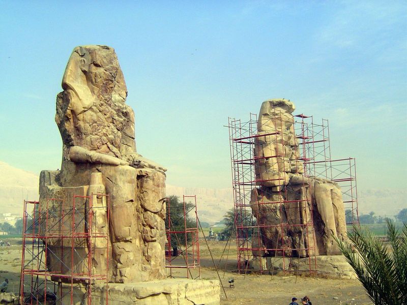 In the distance, cliffs border the Nile Valley; in the foreground the Colossi of Memnon represent Amenophis II, of the 18th dynasty.