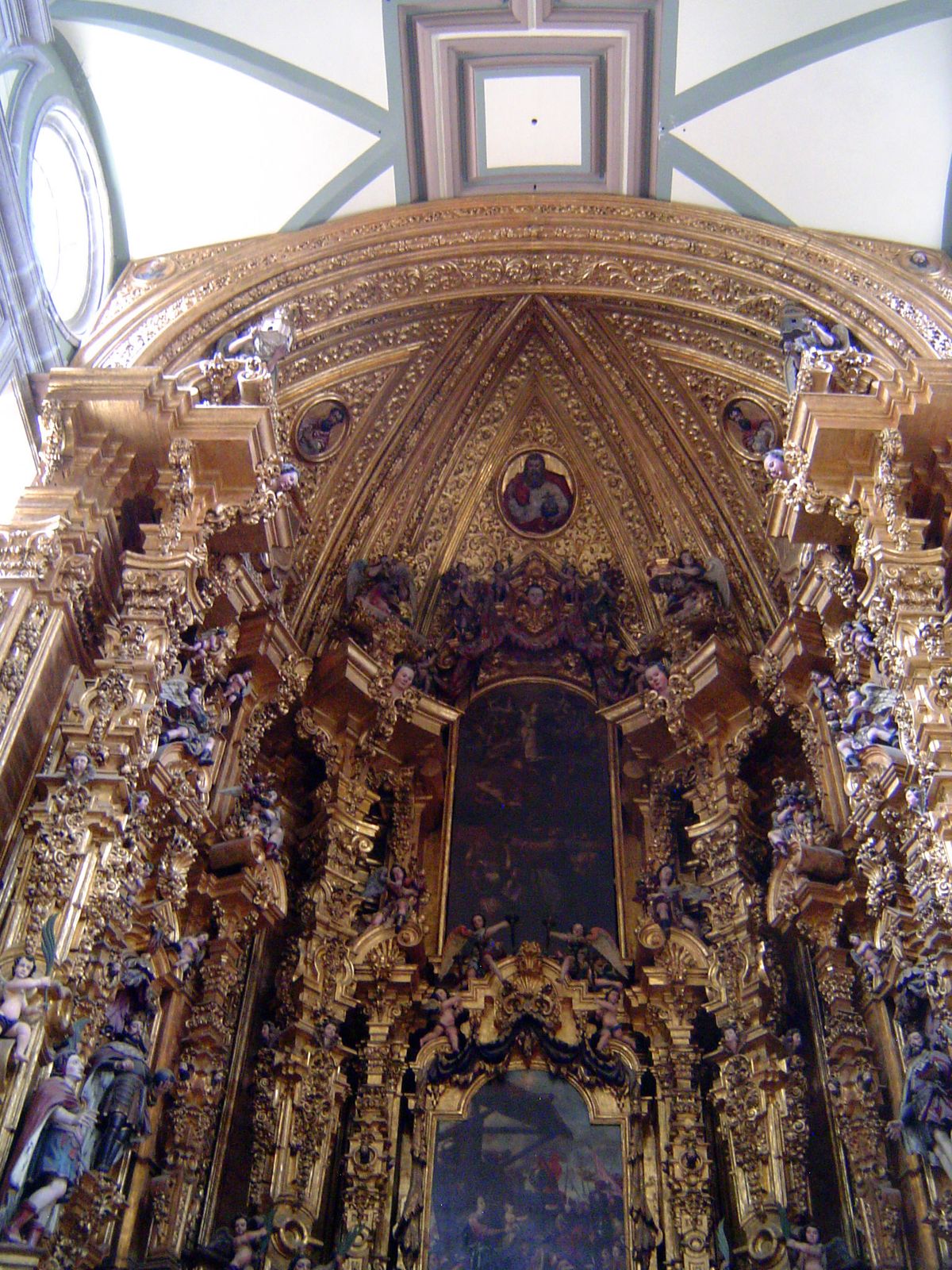 Crowned by God the Father, holding a globe, the altar is filled with saintly figures who appear dark in the midst of the brilliant setting.