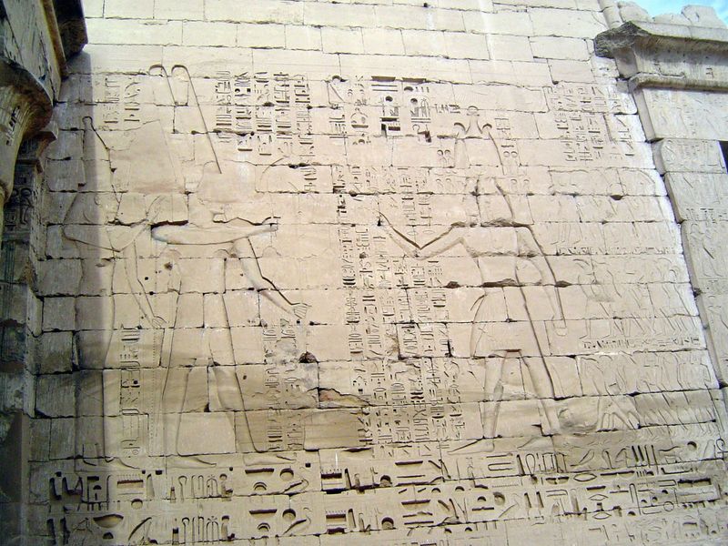 On the west wall of the first court, pharaoh, on the right, offers prisoners of war to Amun-ra and his wife Mut.