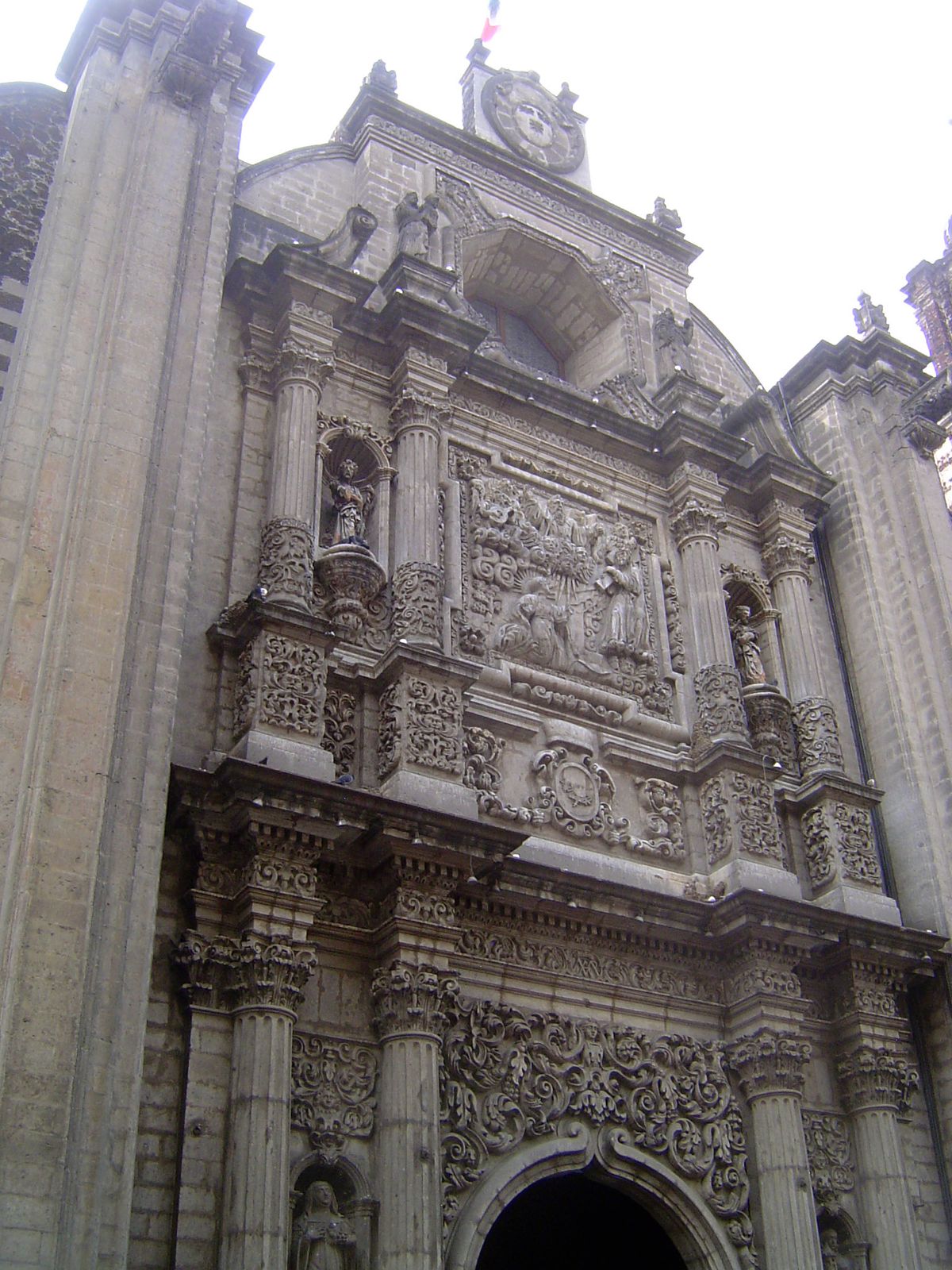 The baroque facade has a central panel showing Christ appearing to St. Ignatius, founder of the Jesuits. The flanking saints squeezed by col