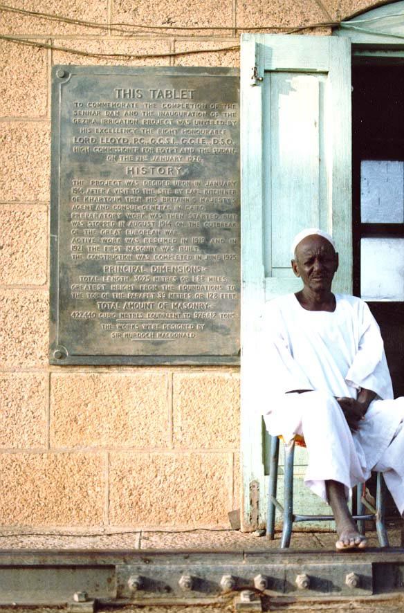 Many miles upstream from Wad Medani, and midway across the Sennar Dam, a guard sits unshaded in the sun, while the tablet behind him recount
