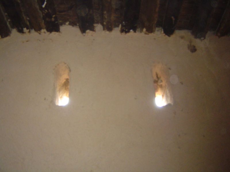 Above, narrow, traditional windows and a palm-log ceiling.