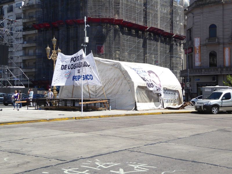 Below the quadriga, a tent is set up by protesters objecting to the closure of an old Pepsico snacks factory in Florida, a crowded Buenos Ai