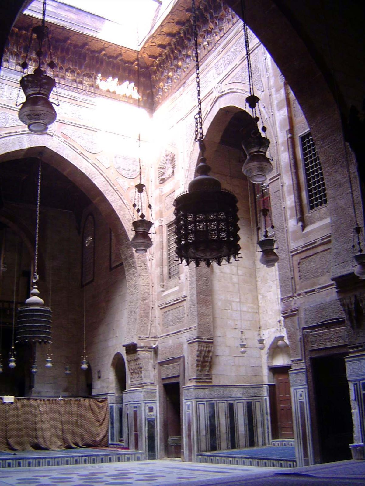 The interior has a cruciform layout; the top of the courtyard is rimmed with a heavy muqarna cornice.