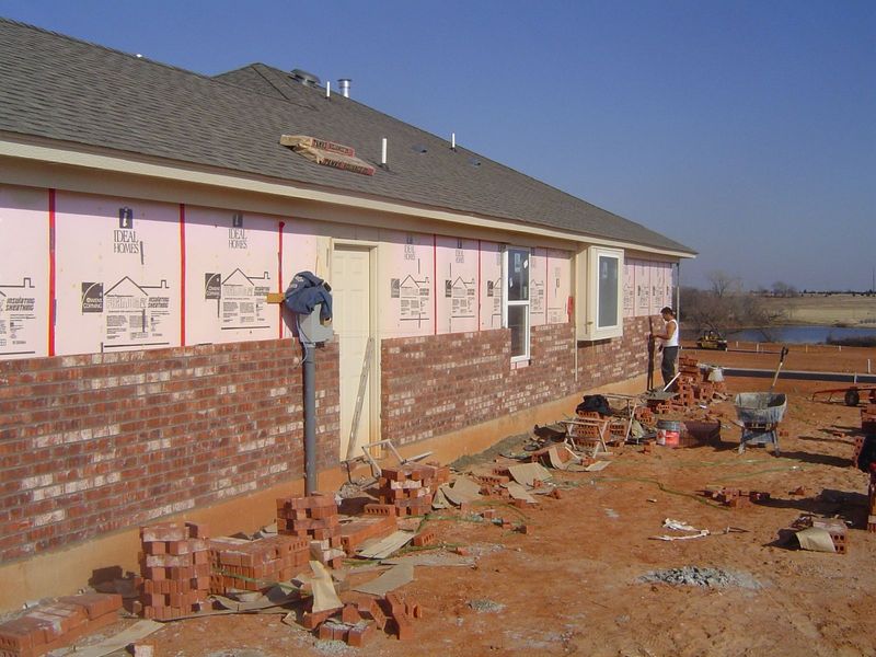 Applying brick veneer. How many hands are involved in building this house? Let's count the tasks or crews: tractor operator, stem wall frame