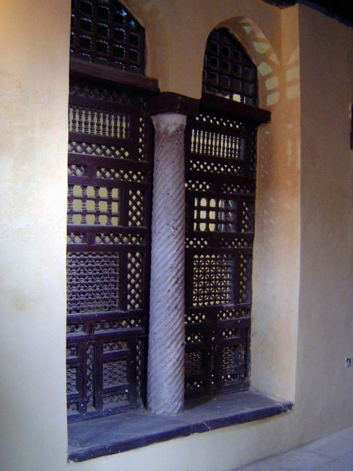 An interior with another ancient column and a wood screen or mashrabiyya.