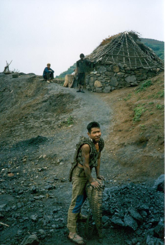 Pausing for breath, a boy leans on the pannier in which he has hauled coal several hundred steps up a dark shaft.