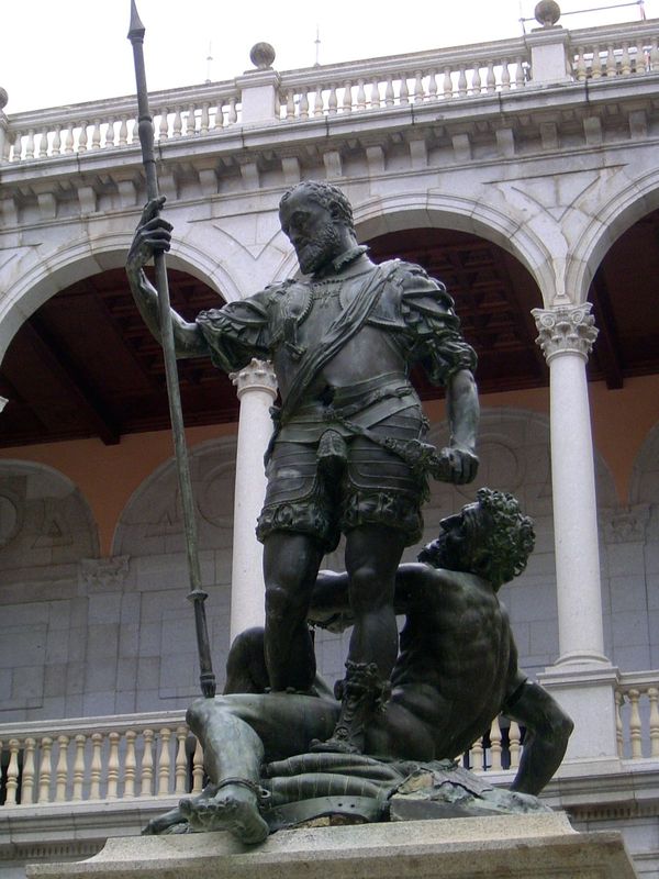Despite the archaic dress, the figure is Alfonso XIII, king of Spain from 1886 until 1941. Here he stands victorious over a chained African 