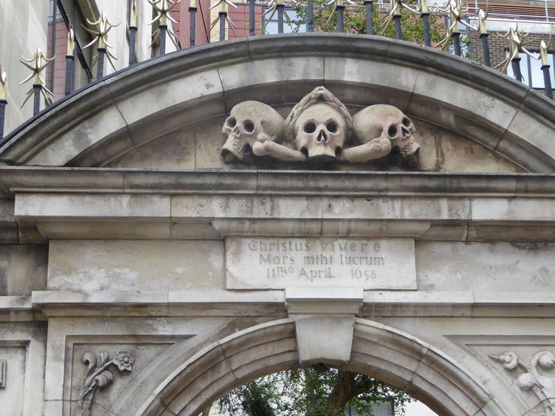 At the entrance, a verse from the Vulgate Philippians 1:21 welcomes death as the reward for those who live in Christ. The skulls above don't