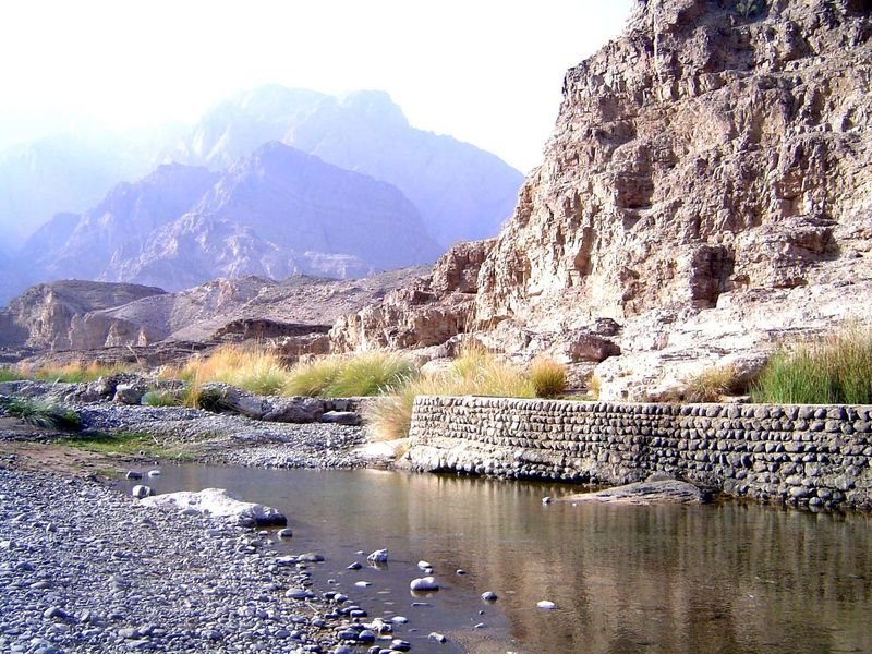 Most of the water is now in the canal behind the stone wall. In the background, the Hajars.