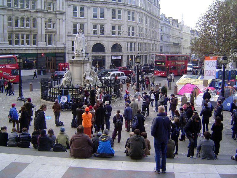 Behind her back, an Occupy London protester rallies the troops.