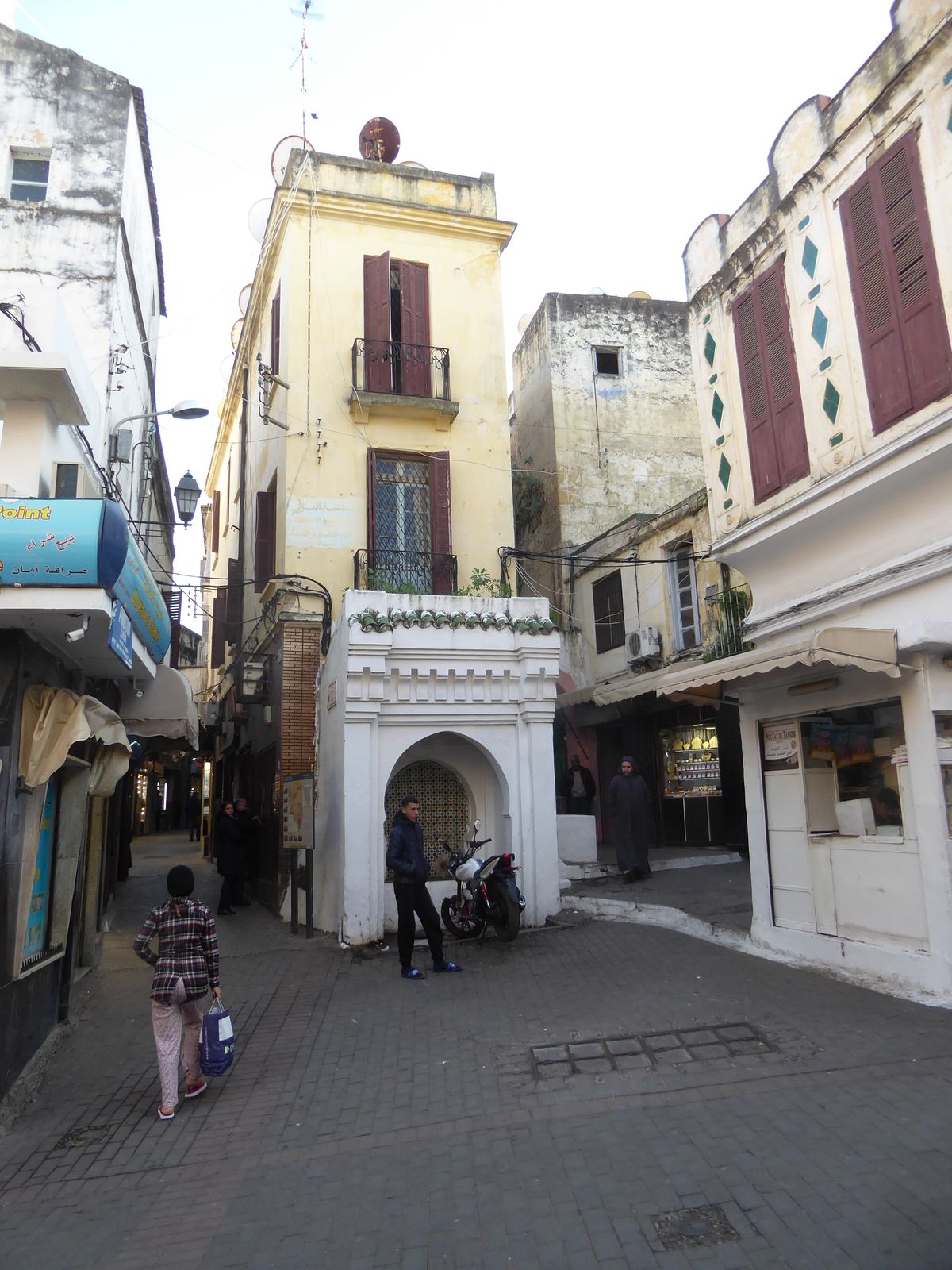 The arch leads to the Rue de Saghins. The motorcycle is parked in front of the Seqaya or Fountain Siaghin, another dried-up fountain. Accord