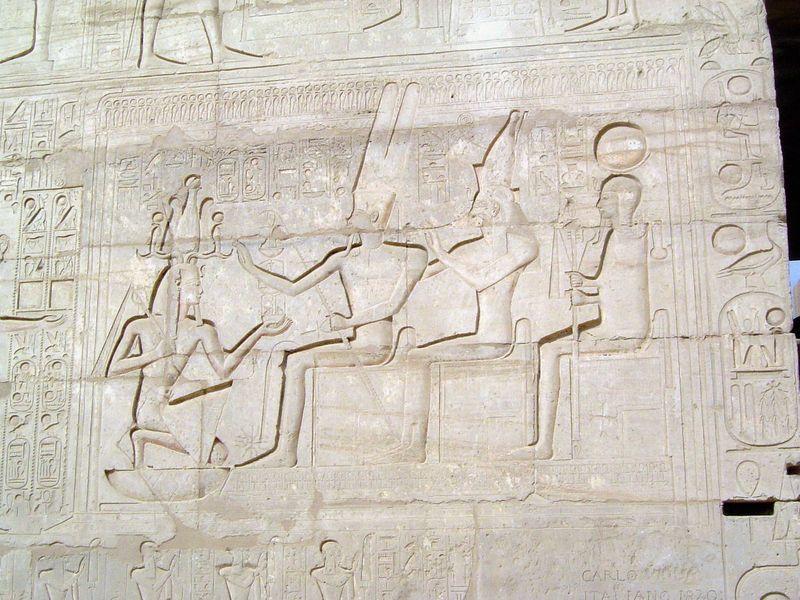 Meanwhile, Rameses II kneels before the Theban triad, Amun-Ra, Mut, and Khonsu.