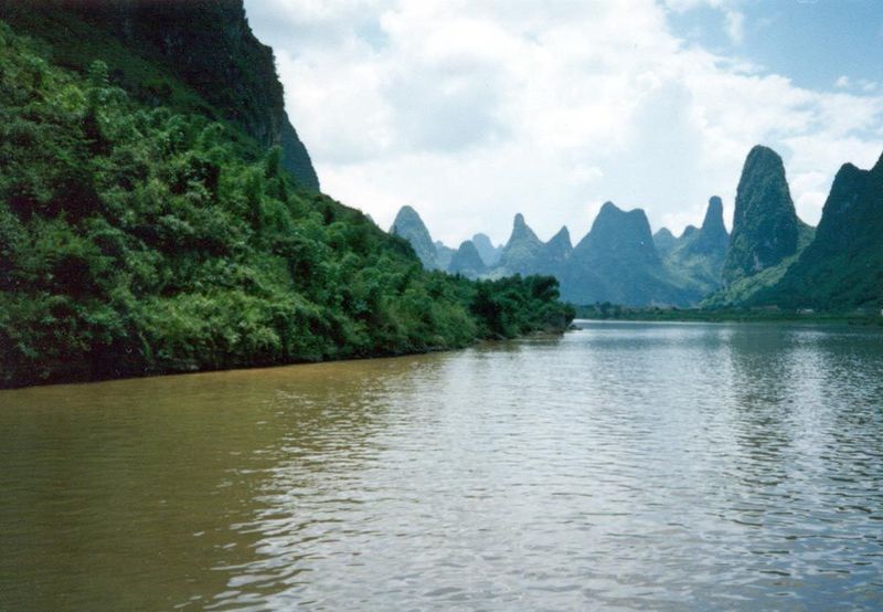 Tourist boats cruise downstream through karst towers. A thick layer of calcium carbonate has dissolved along joints and fissures and left th