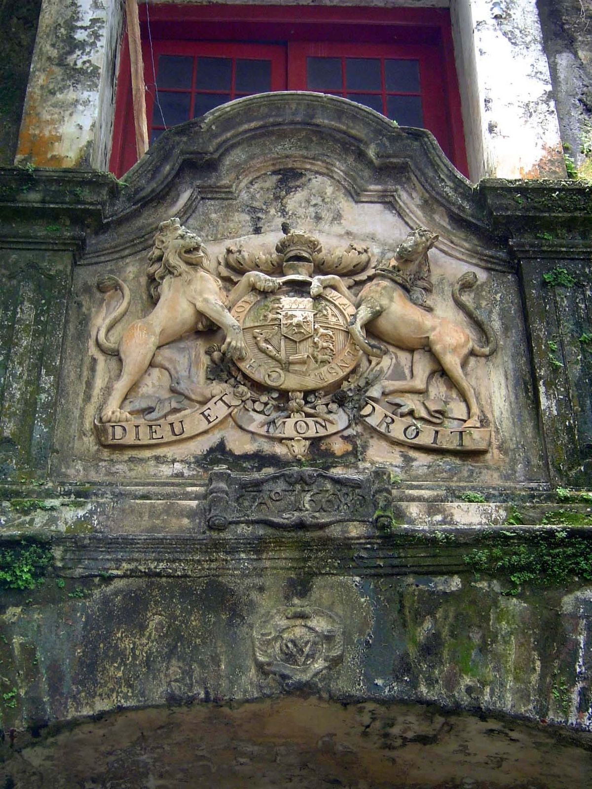 The British coat-of-arms is a 19th century addition; on the cornerstone below you see the earlier logo of the VOC, for the United East India