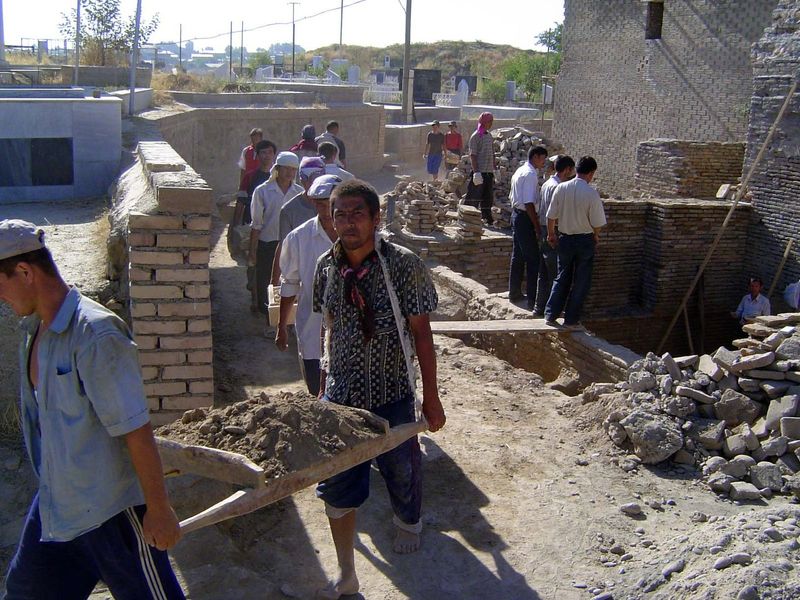 At the far side of the cemetery, construction workers is moving earth the old-fashioned way.