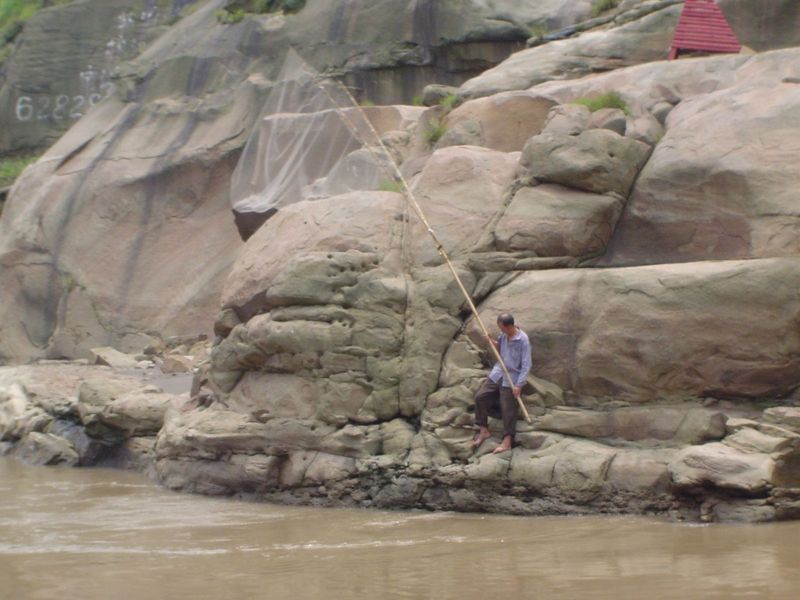 Ignoring all the progress, a fisherman handles his net on the rocky bank. Some 60% percent of all the freshwater fish caught in China—chiefl