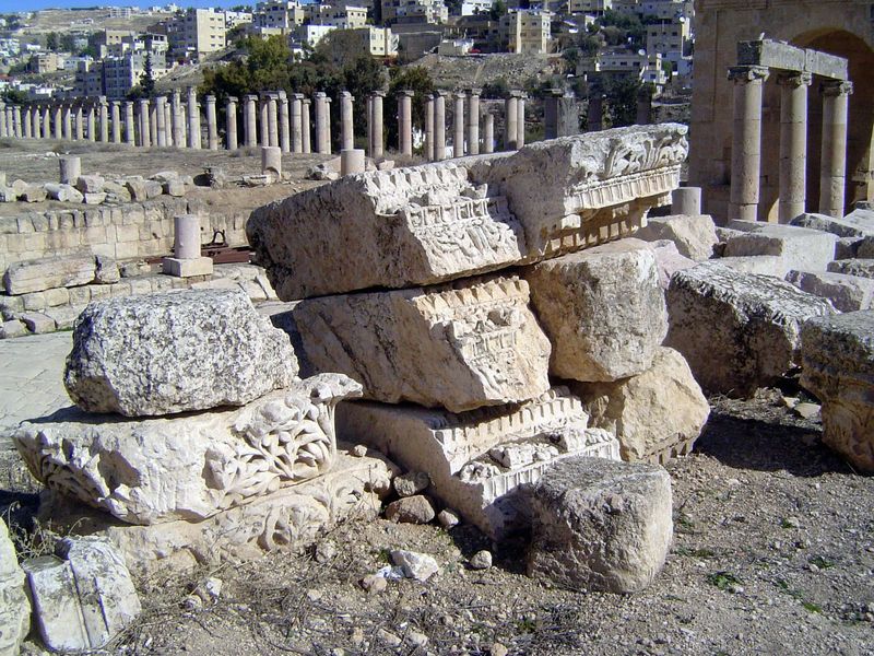 Cornice blocks awaiting reassembly. The cardo continues north between the columns; the second decumanus crosses under the archway at the rig