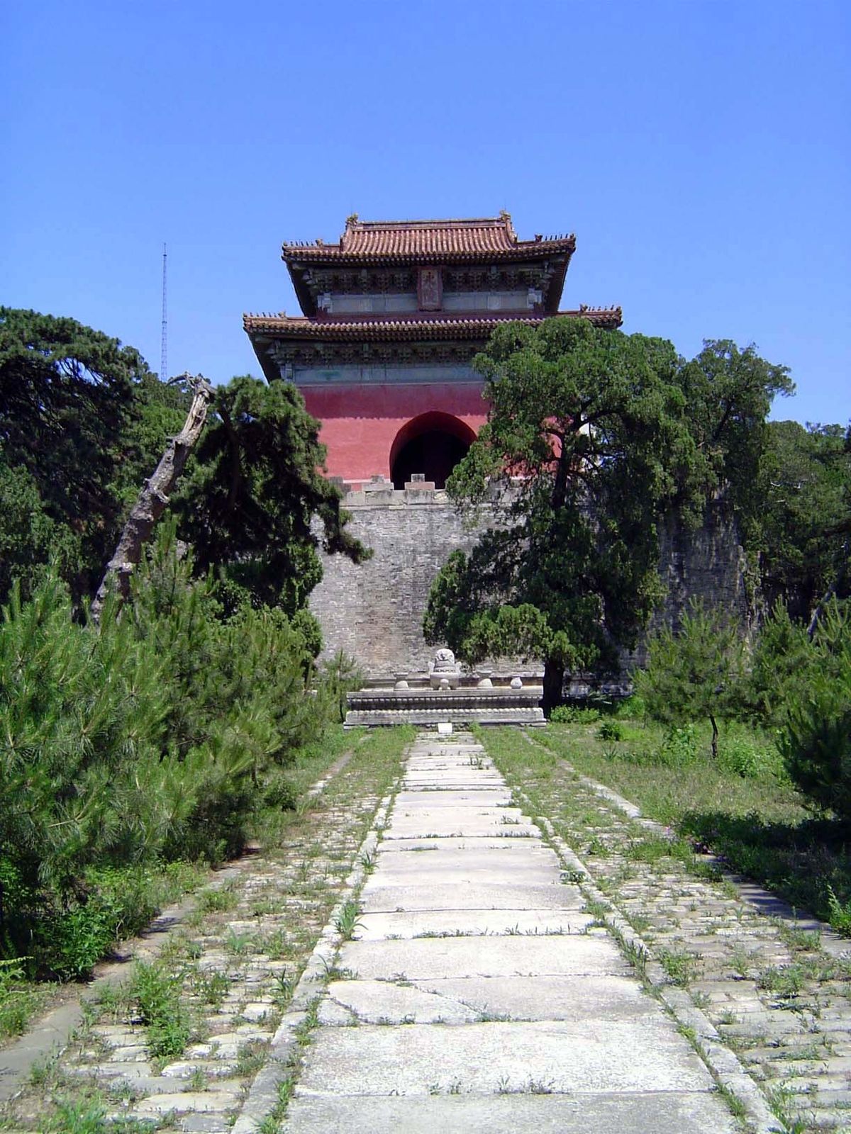 The vermilion soul tower sits on a dark rampart or base. In front of it and at the end of the path there's a stone incense burner.
