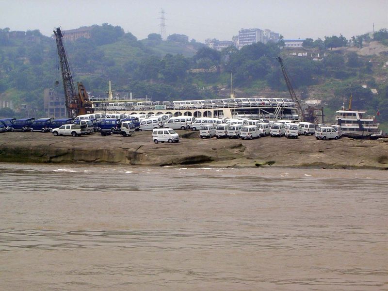 A mile or so downstream: new Changan vans are parked on the shore. Behind them is the ship that's going to take them downstream.