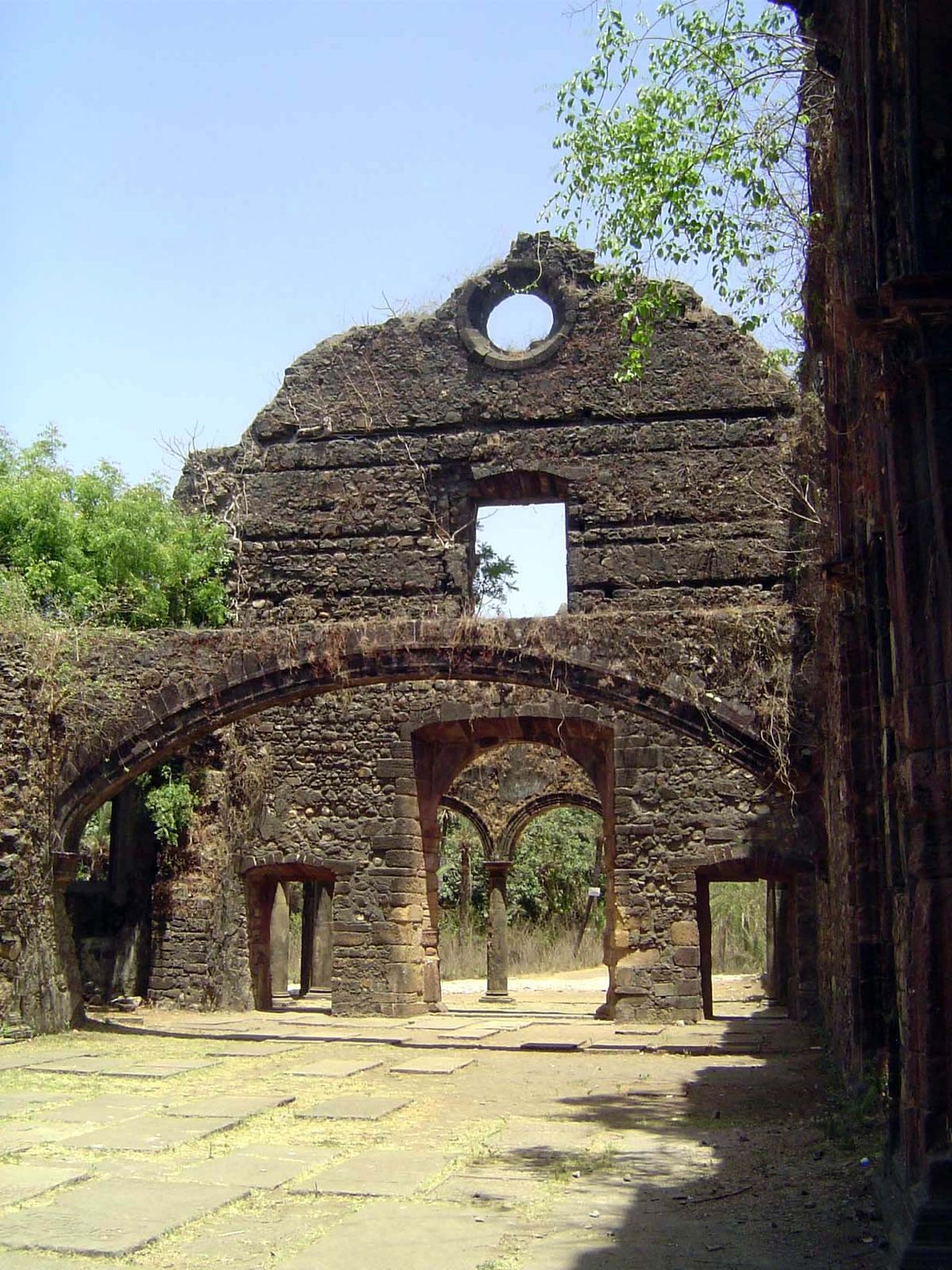The walls are of cut laterite. The floor is paved with tombstones. The arch once supported the choir.