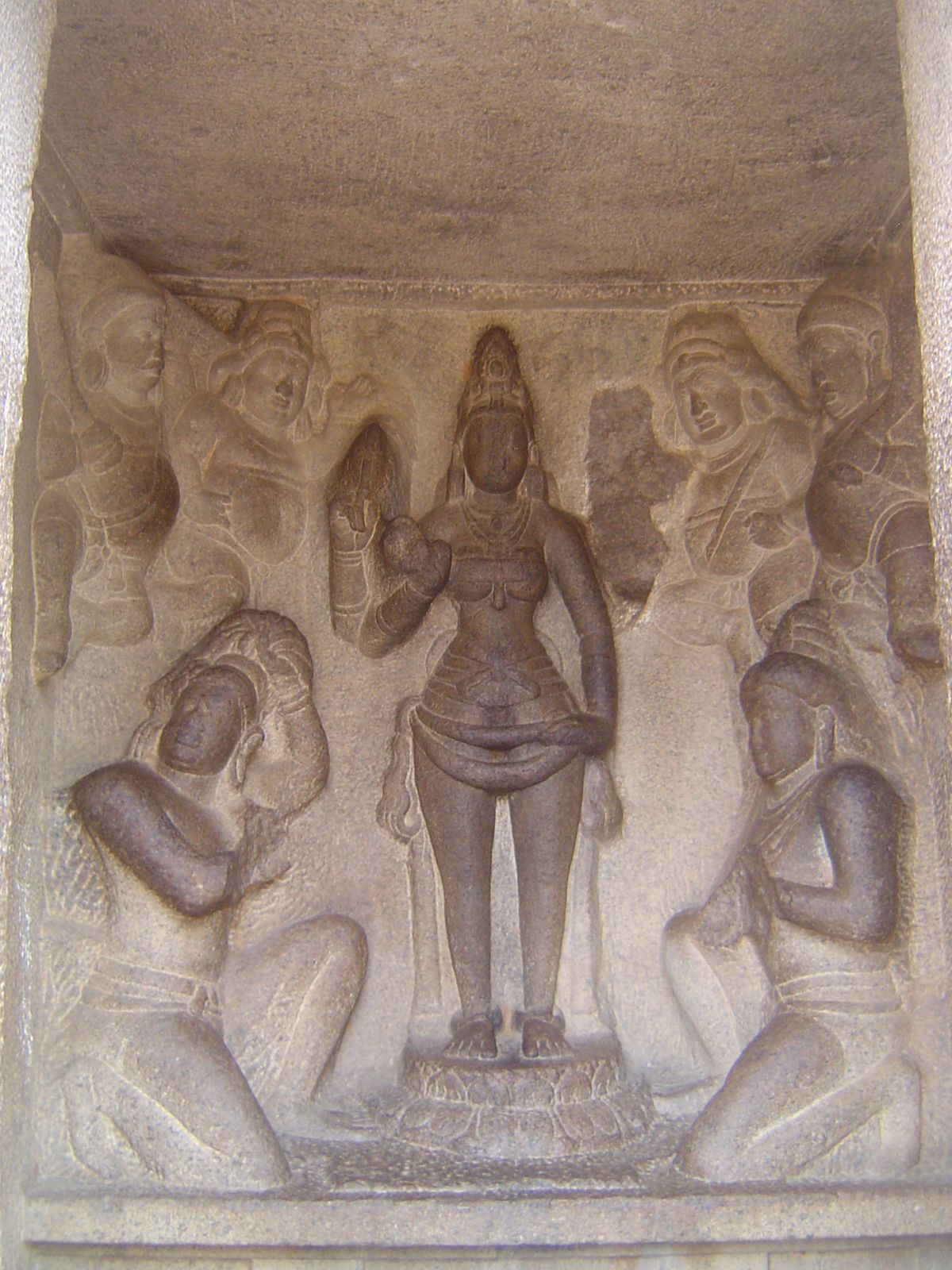 Inside the shrine, Durga and her ganas or attendants stand before two devotees. One prepares to cut off his head, while the other hopes that
