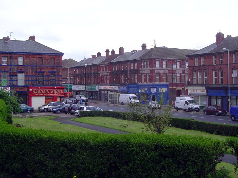 A commercial district in a residential area: Stanley Road in the suburb of Bootle. The camera is near a statue surveying the street.