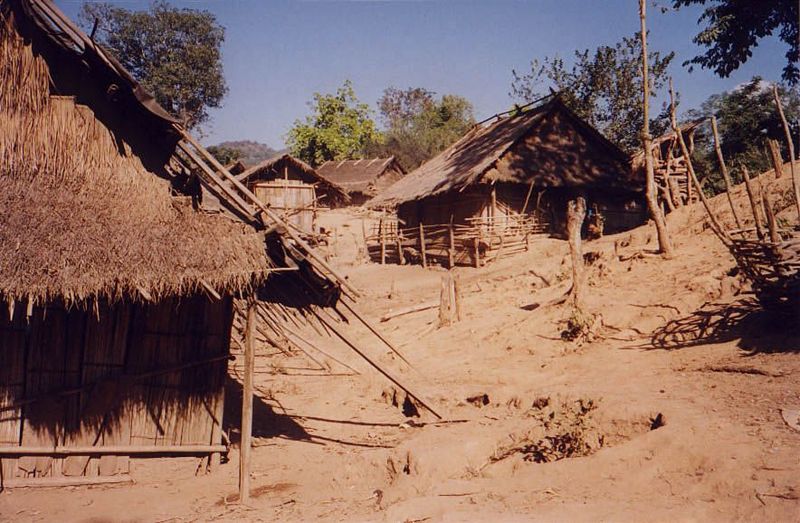 A stranger Walks circumspectly around a cluster of houses whose barren site contrasts with the surrounding forest.